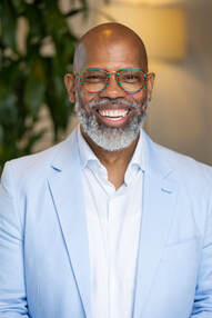 Curtis Hill, a black man with a big engaging smile, bald with grey moustache and beard wearing large frame glasses, white shirt and light blue sport coat.